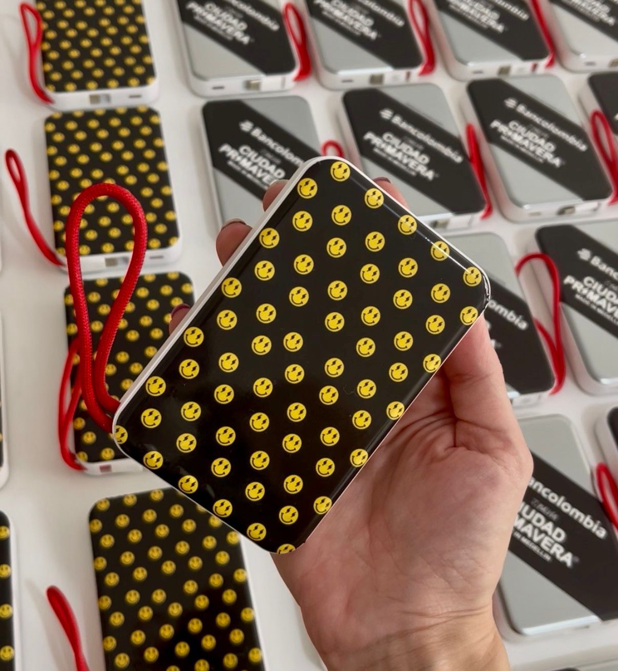 Powerbank con patrón de smileys amarillos sostenida sobre la línea de producción