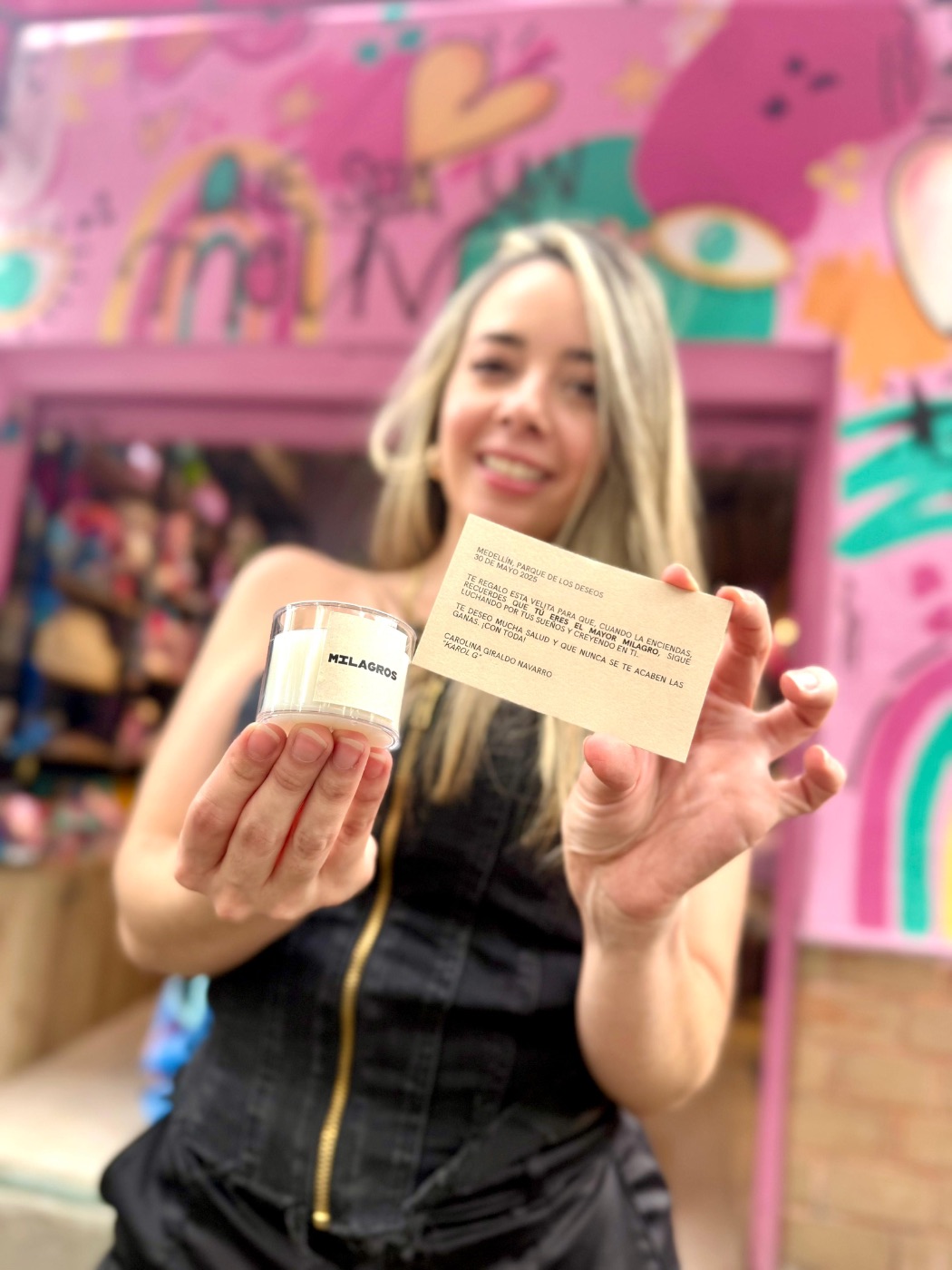 Mujer sosteniendo vela Milagros y tarjeta firmada por Karol G durante el evento